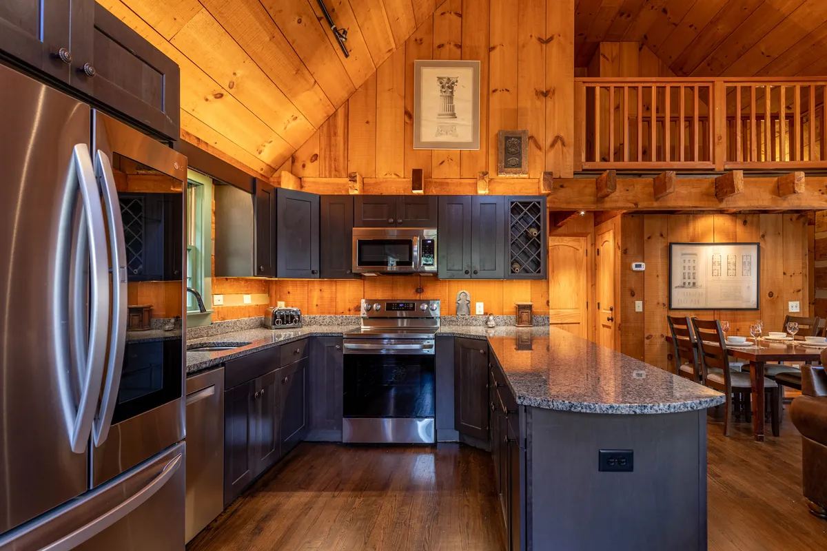 A modern, well-equipped kitchen featuring a granite countertop, stainless steel appliances, visible wooden beams, and an adjoining dining area, all bathed in warm, inviting light. The kitchen is open to the main living space, emphasizing both culinary potential and opportunities for social cooking and dining.