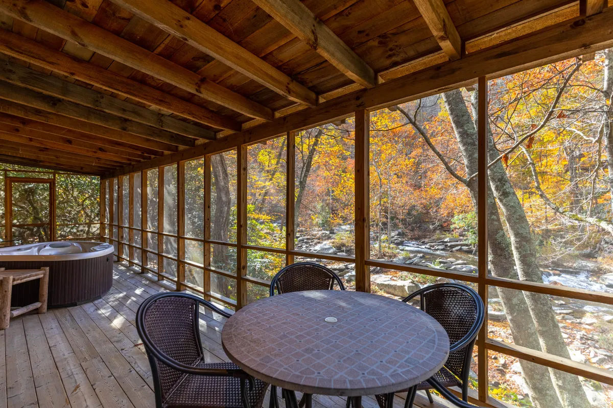 This calm indoor scene centers on a hot tub and a round table by large windows, with autumn foliage visible outside. The space is designed for both quiet relaxation and socializing, offering views of seasonal changes and direct visual connection to the outdoors.