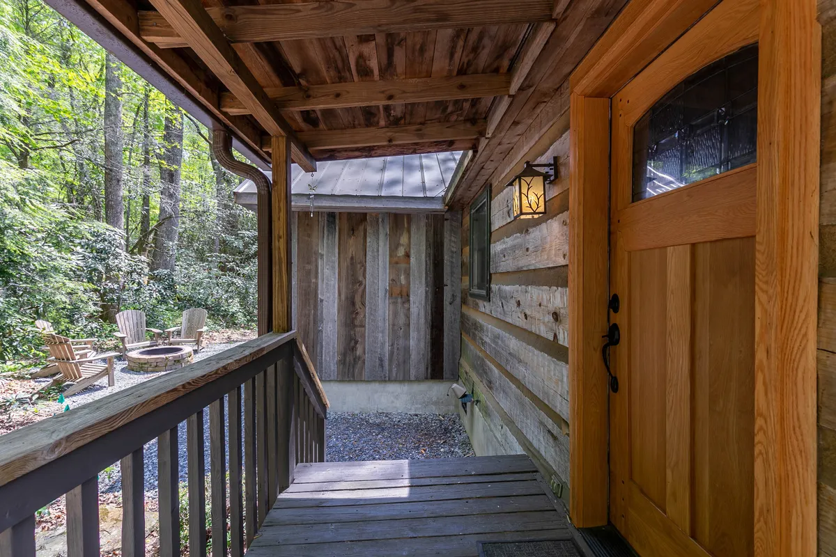 A welcoming exterior shot of the cabin's front porch, featuring adirondack chairs and surrounding greenery. There’s a sense of privacy and warmth, with a hint of sunset light and the promise of cozy evenings.