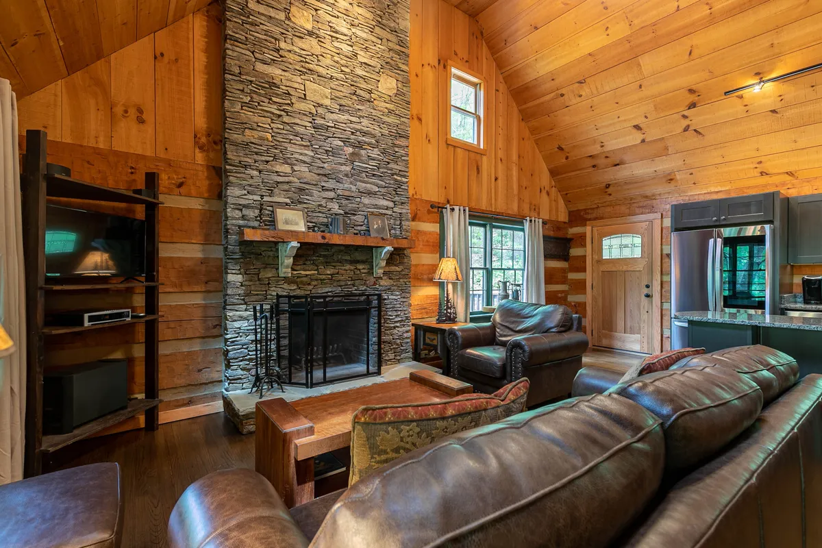 A cozy living area featuring a prominent stone fireplace, exposed wooden beams, and leather sofas arranged around a coffee table. The space is set for relaxing evenings, socializing, or enjoying family gatherings, with a warm and welcoming atmosphere.