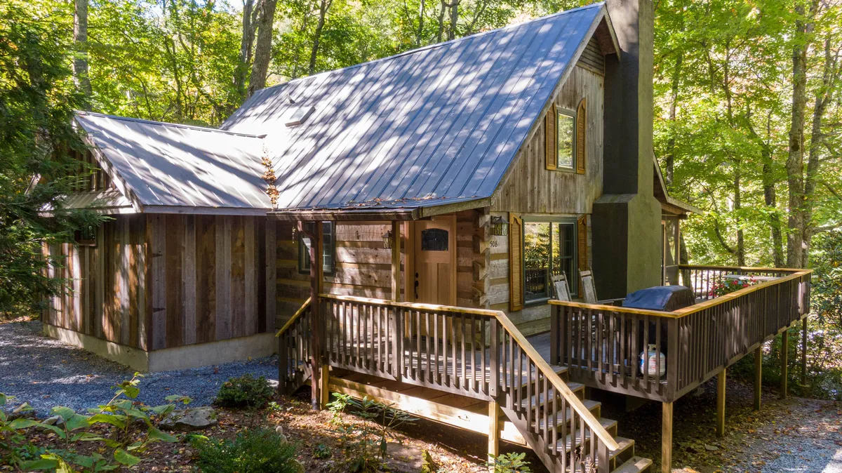 A cozy wooden deck with a slanted roof and large windows, surrounded by natural woodland. The setting is inviting for relaxing outdoors, hosting gatherings, or simply soaking up the tranquil environment with your pet.